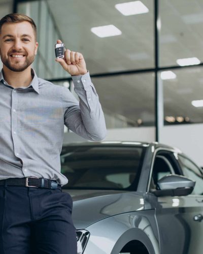 Young man holding car keys by his new car