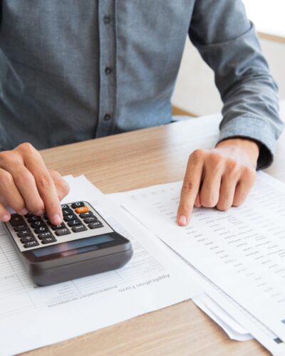 Close-up of unrecognizable man working with financial data. He using calculator and examining document. Financial inspector holding examination. Paperwork or finance concept
